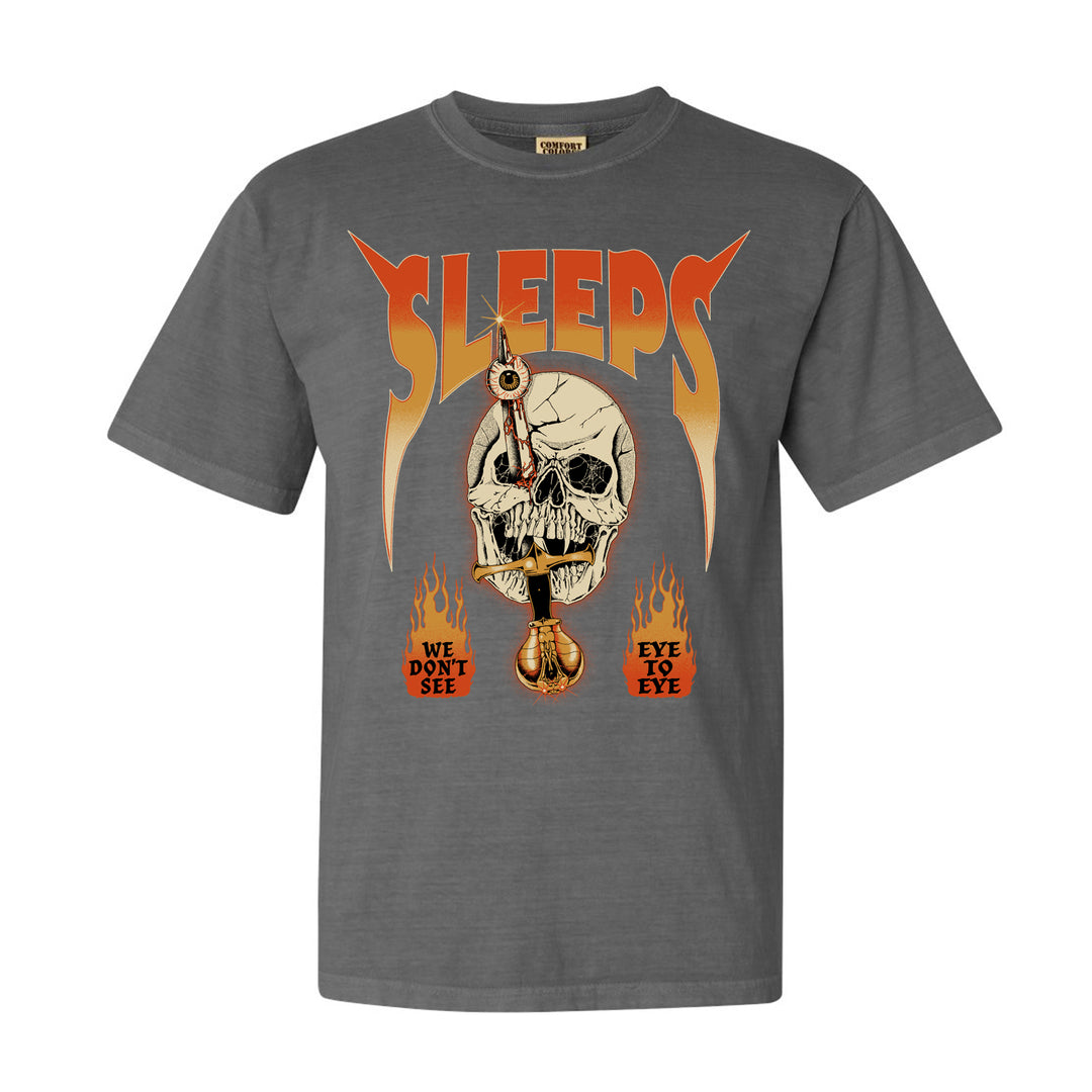 While She Sleeps Comfort Colors garment-dyed gray tee with cracked skull and dagger, bold orange SLEEPS text, WE DONT SEE EYE TO EYE over flames. Made from soft ring-spun cotton for comfort.