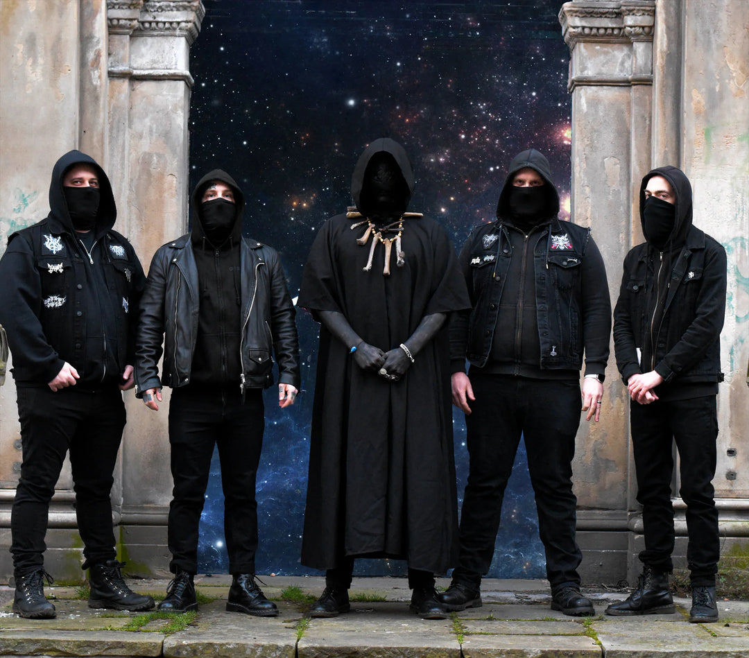 Five people dressed in black, some hooded and masked, stand in front of stone pillars with a starry space background behind them. The central figure wears a long cloak and gloves.