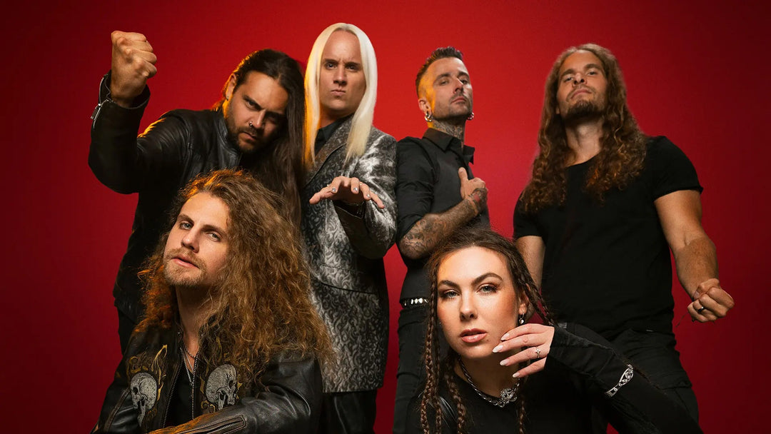 Six band members are lying in a circle on a wooden floor, looking up, with the bands logo AMARANTHE displayed on a black background beside them.