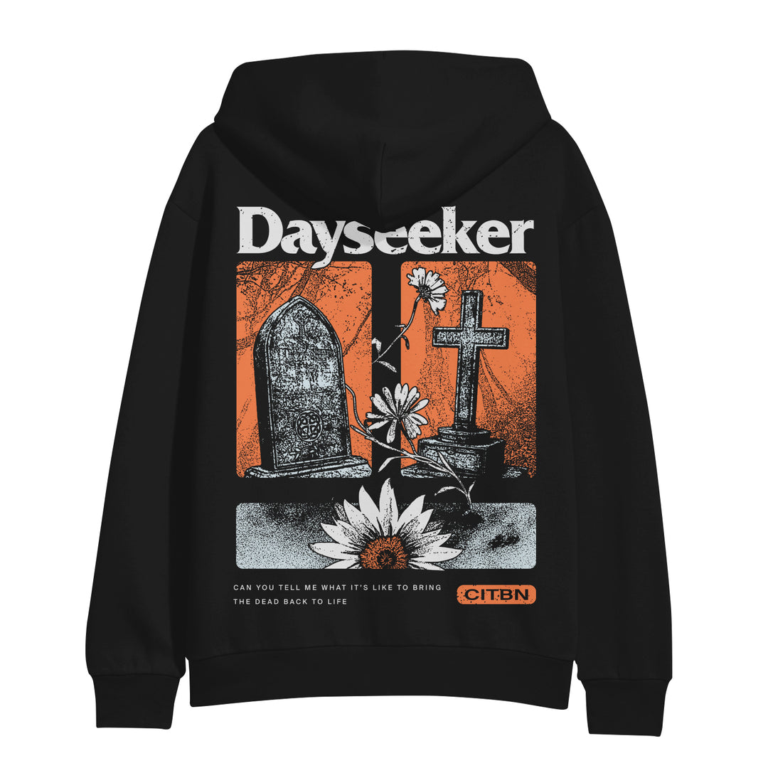 Dayseeker black hoodie features bold white “Dayseeker” text at the top, a black gravestone, cross, flowers, and lotus on a red background. Bottom text reads: Can you tell me what it’s like to bring the dead back to life.