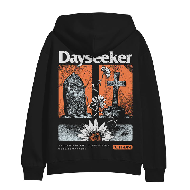Dayseeker black hoodie features bold white “Dayseeker” text at the top, a black gravestone, cross, flowers, and lotus on a red background. Bottom text reads: Can you tell me what it’s like to bring the dead back to life.