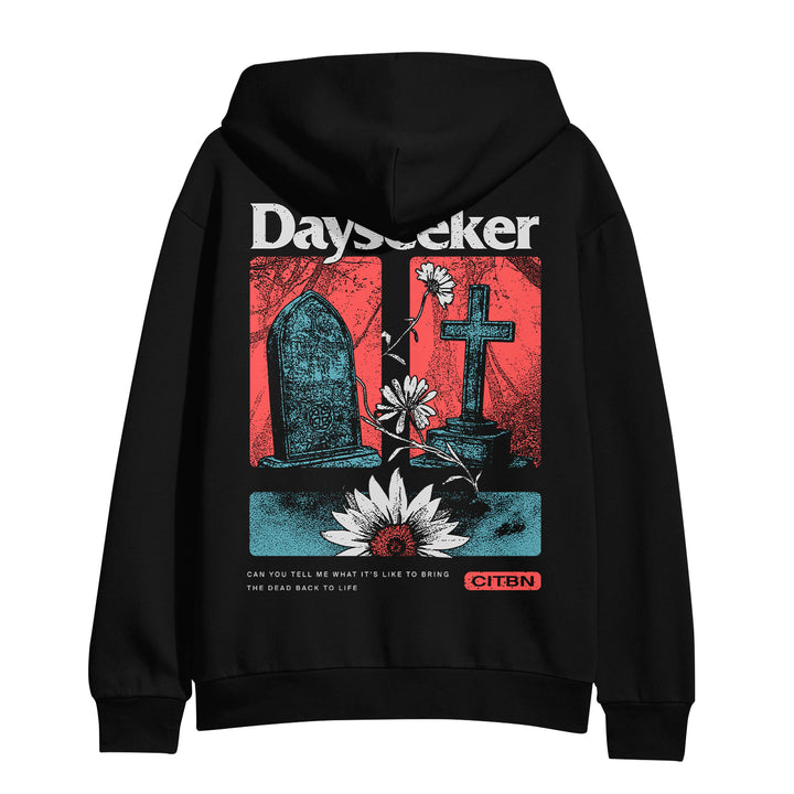Dayseeker black hoodie features bold white “Dayseeker” text at the top, a black gravestone, cross, flowers, and lotus on a red background. Bottom text reads: Can you tell me what it’s like to bring the dead back to life.