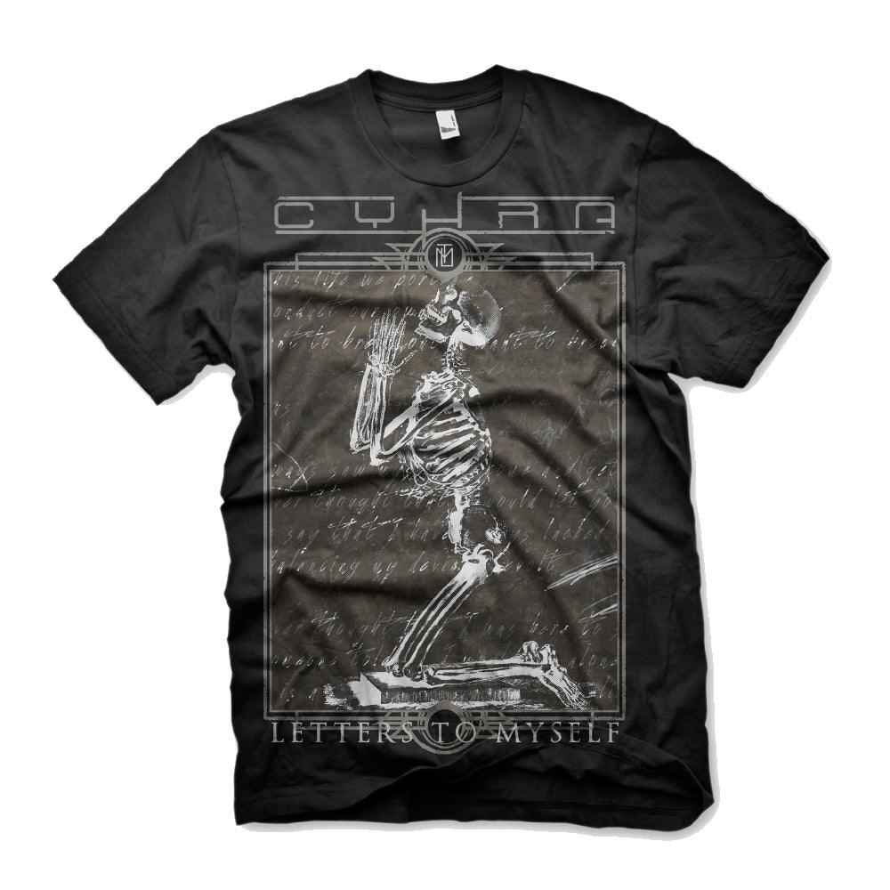 image of a black tee shirt on a white background. tee has full body print of a praying skeleton